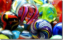 Close-up shot of brightly colored glass marbles of varying designs, including classic cat's eye, swirling rainbow patterns, and twisting, psychedelic shapes and colors