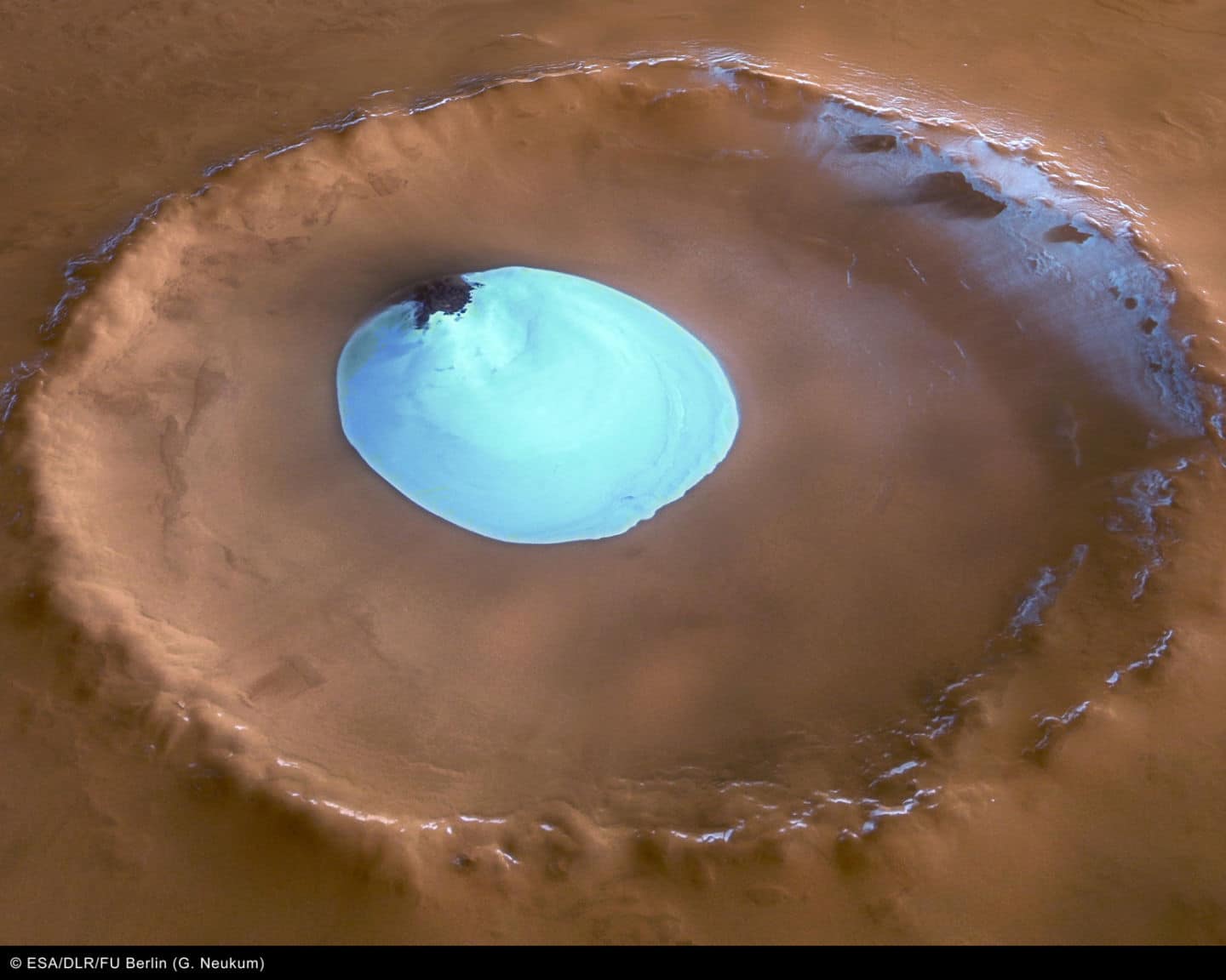 Vista de un cráter sin nombre en las latitudes septentrionales de Marte. El cráter tiene 35 km de ancho y una profundidad máxima de aproximadamente 2 km por debajo del borde del cráter. El parche circular de material brillante ubicado en el centro del cráter es hielo de agua residual.